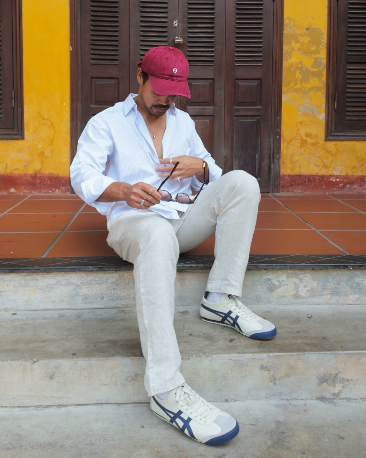 Ron seated on a step in Hoi An's old town, linen shirt and trousers, cream and navy sneakers