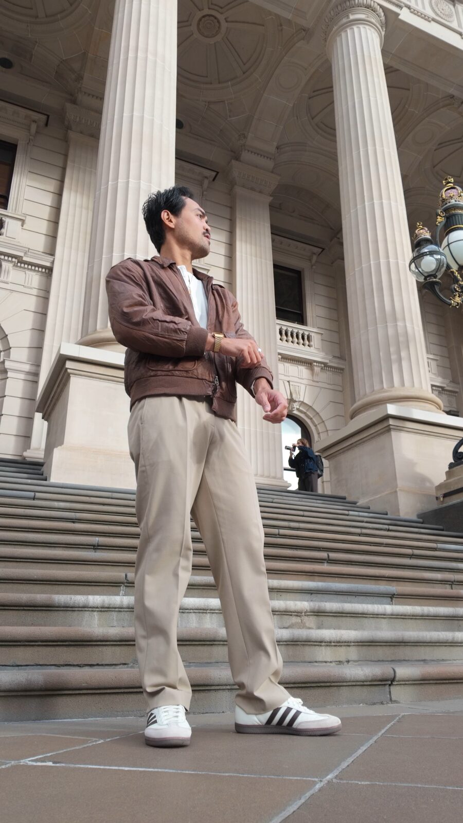 Ron on the steps of Parliament House Melbourne in a worn brown leather flight jacket and stone pleated trousers